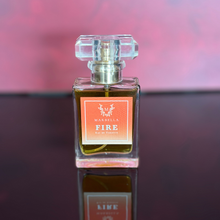 Load image into Gallery viewer, Perfume bottle labeled 'Fire' by Marbella on a reflective surface with a blurred background

