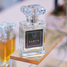 Load image into Gallery viewer, Perfume bottle labeled 'Earth' by Marbella on a wooden stand with a blurred background
